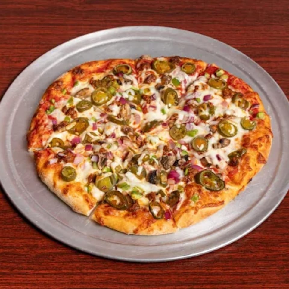 A whole pizza with jalapeños, red onions, and meat toppings on a metal pan.