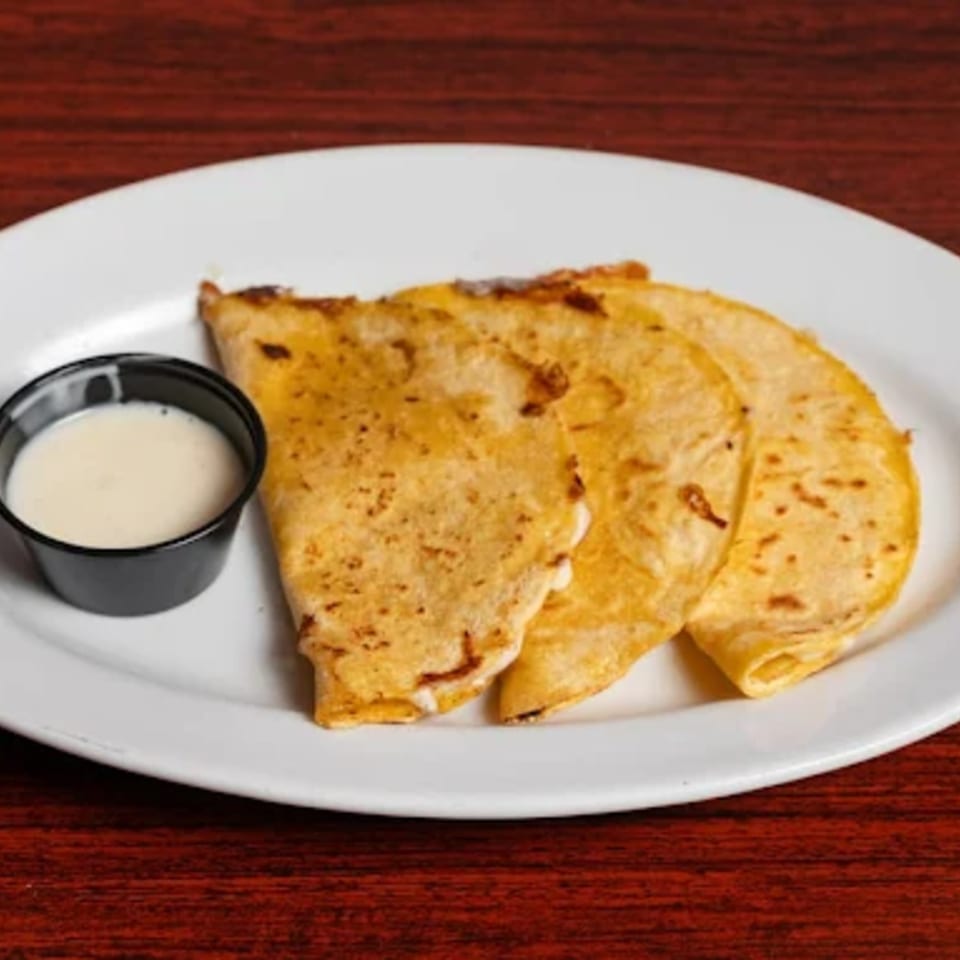 Three golden-brown quesadillas with a side of white dipping sauce on a white plate.